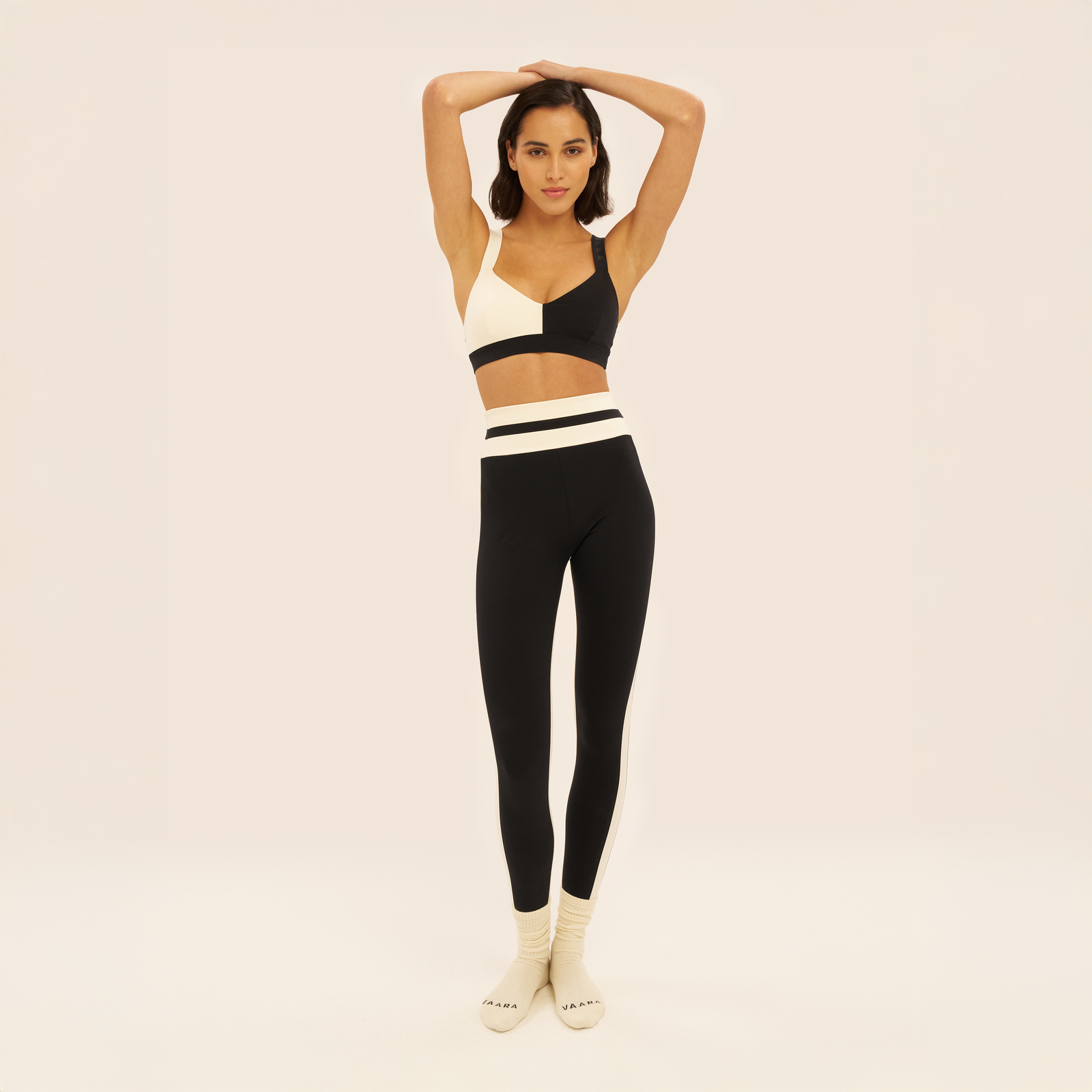 Woman wearing a black and white sports bra and leggings set on a beige background